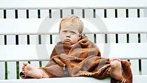 a little one-year-old girl, wrapped in a towel, with a dirty face, lonely sitting on a swing in the garden, in the