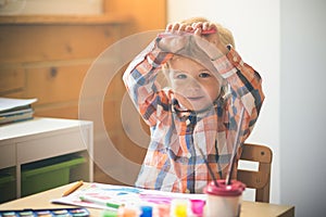 Little painter happily looks at camera. Developing activity for children in preschool age. Boy draw with help of colours