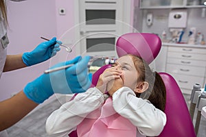 little patient covers her mouth her hands and does not allow dentist to look into her mouth.