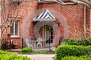 Little patio with iron railings on brick house - Stiped awning over door with wreath and chiminea and white iron bistro set -