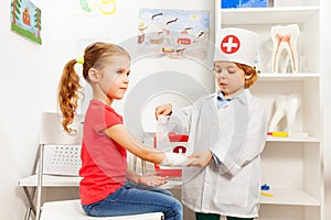 Little pediatrician doctor bandaging girl's arm