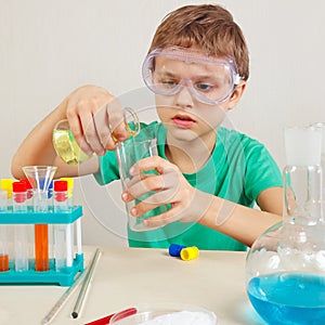 Little pensive boy in safety goggles doing chemical experiments in laboratory