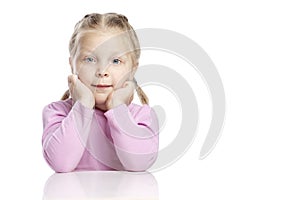 Little pensive girl with pigtails sits at a table and dreams. Isolated on a white background