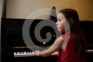 Little pianist musician girl playing piano and singing song, creating music, performing and composing melody on the