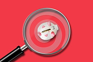 Little piggy bank on a red background. View through a magnifying glass. Decrease in accumulations. Business.