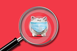 Little piggy bank on a red background. View through a magnifying glass. Decrease in accumulations. Business