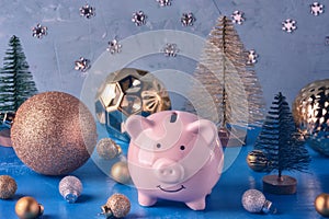 Little pink piggy bank in a magical forest of Christmas balls and decorative Christmas trees.