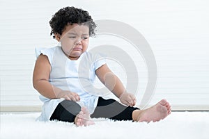 Little pitiful African American chubby kid girl is crying with tears drop from eyes while sitting on fluffy carpet on floor