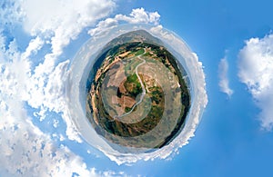 Little planet view from aerial drone of fields and winding roads, farms, harvested grass, haystacks. Wind turbines in mountain,