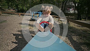 Little playful blond girl rides teeter totter at playground