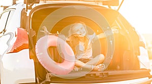 Little pleasured girl sitting in a car trunk on a travel vacation