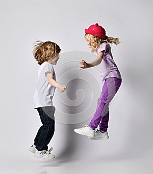 Little positive blond baby girl and boy sister and brother in stylish casual clothing and accessories jumping and having fun