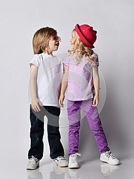 Little positive blond baby girl and boy in stylish casual clothing and accessories standing and looking at each other