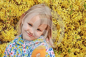 Little positive girl 5 years old, blonde, smiling cheerfully, portrait against a background of brightly blossoming yellow flowers