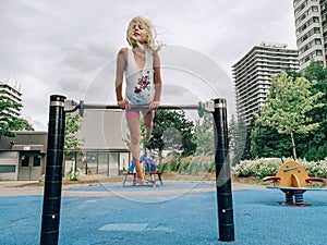 Little preschool blonde Caucasian girl hanging upside down on pullup bar on playground
