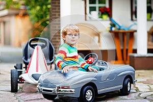 Little preschool boy driving big toy car and having fun, outdoors. Happy child play and having outdoor activity. Kid