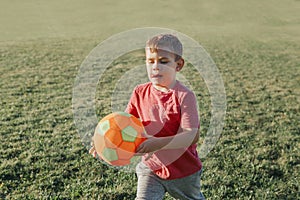 Little preschool Caucasian boy playing soccer football on playground outside. Kid carrying holding ball. Happy authentic candid