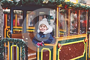 Little preschool girl on a carousel train at Christmas funfair or market, outdoors. Happy child having fun. Traditional