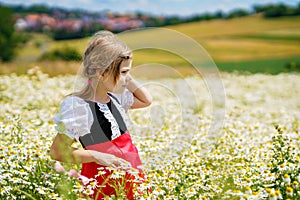 Little preschool girl in daisy flower field. Cute happy child in red riding hood dress play outdoor on blossom flowering