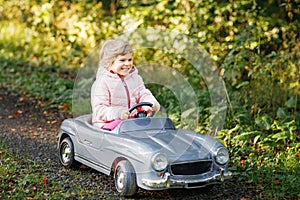 Little preschool girl driving big vintage toy car. Happy child having fun with playing outdoors. Active preschooler