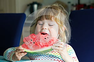 Little preschool girl eating fresh red watermelon. Toddler child bites in ripe healthy fruit. Kid enjoying snack in