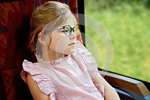 Little preschool girl with glasses sitting in train and looking out of window while moving. Happy child , smiling child