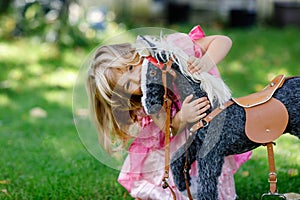 Little preschool girl hugging with rocking horse toy. Happy child in princess dress on sunny summer day in garden. Girl