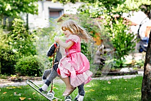 Little preschool girl hugging with rocking horse toy. Happy child in princess dress on sunny summer day in garden. Girl