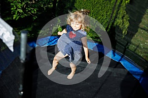 Little preschool girl jumping on trampoline. Happy funny toddler child having fun with outdoor activity in summer