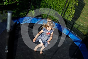 Little preschool girl jumping on trampoline. Happy funny toddler child having fun with outdoor activity in summer