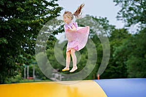 Little preschool girl jumping on trampoline. Happy funny toddler child having fun with outdoor activity in summer