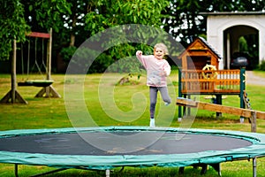 Little preschool girl jumping on trampoline. Happy funny toddler child having fun with outdoor activity in summer