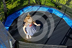 Little preschool girl jumping on trampoline. Happy funny toddler child having fun with outdoor activity in summer