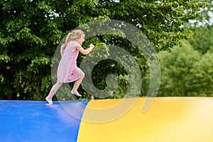 Little preschool girl jumping on trampoline. Happy funny toddler child having fun with outdoor activity in summer photo