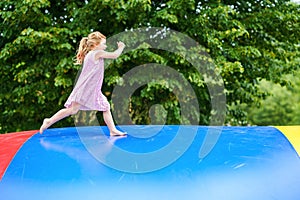Little preschool girl jumping on trampoline. Happy funny toddler child having fun with outdoor activity in summer