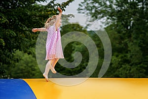 Little preschool girl jumping on trampoline. Happy funny toddler child having fun with outdoor activity in summer photo