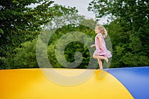 Little preschool girl jumping on trampoline. Happy funny toddler child having fun with outdoor activity in summer photo