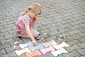 Little preschool girl painting with colorful chalks on ground on backyard. Positive happy toddler child drawing and creating