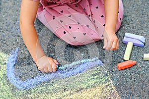 Little preschool girl painting rainbow with colorful chalks on ground on backyard. Positive happy toddler child drawing