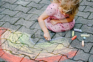 Little preschool girl painting rainbow with colorful chalks on ground on backyard. Positive happy toddler child drawing