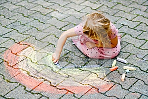 Little preschool girl painting rainbow with colorful chalks on ground on backyard. Positive happy toddler child drawing and