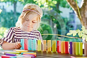 Little preschool girl playing board game with colorful bricks domino. Happy child build tower of wooden blocks