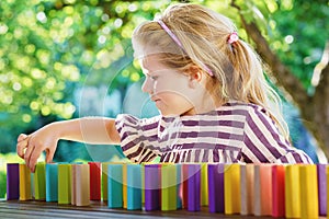 Little preschool girl playing board game with colorful bricks domino. Happy child build tower of wooden blocks