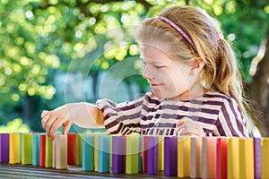 Little preschool girl playing board game with colorful bricks domino. Happy child build tower of wooden blocks