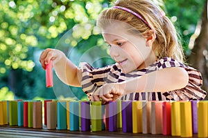 Little preschool girl playing board game with colorful bricks domino. Happy child build tower of wooden blocks