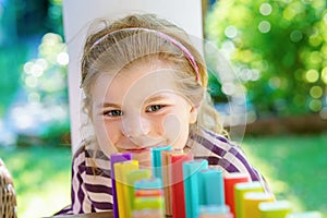 Little preschool girl playing board game with colorful bricks domino. Happy child build tower of wooden blocks