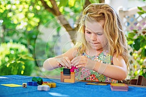 Little preschool girl playing board game with colorful bricks. Happy child build tower of wooden blocks, developing fine