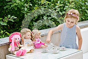 Little preschool girl playing with dolls. Happy excited child play tea party with toys. Role games for children