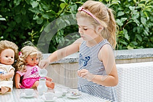 Little preschool girl playing with dolls. Happy excited child play tea party with toys. Role games for children