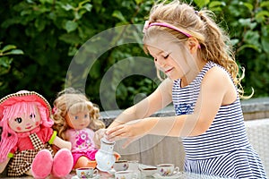 Little preschool girl playing with dolls. Happy excited child play tea party with toys. Role games for children